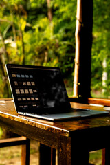 Laptop and cup on wooden table of terrace with tropical forest view at sunset, remote work digital nomad