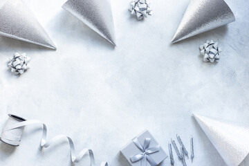 Holiday festive party flat lay with silver carnaval caps and cake candles, top view. Gift box and streamers on gray stone background