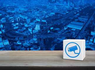 Cctv camera flat icon on white block cube on wooden table over modern city tower, street, expressway and skyscraper, Technology security and safety online concept