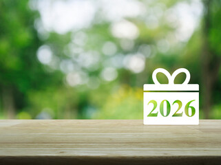 Gift box happy new year 2026 flat icon on wooden table over blur green tree in park, Business happy new year 2026 shopping concept