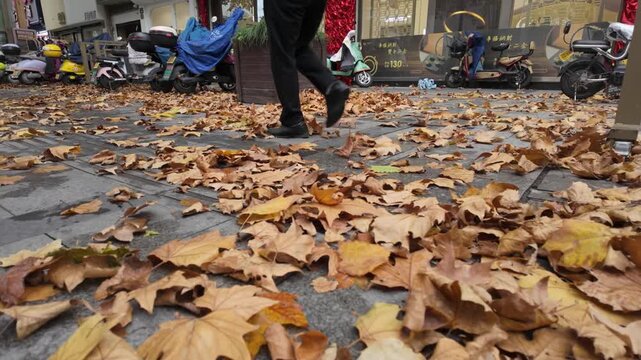 Pedestrians walk through streets covered in fallen leaves
