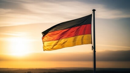 The German flag waves against a sunset backdrop over a body of water and distant land