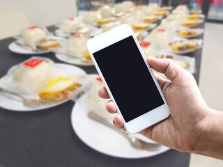 Hand holding mobile phone over abstract blurred background of snack set for coffee break.