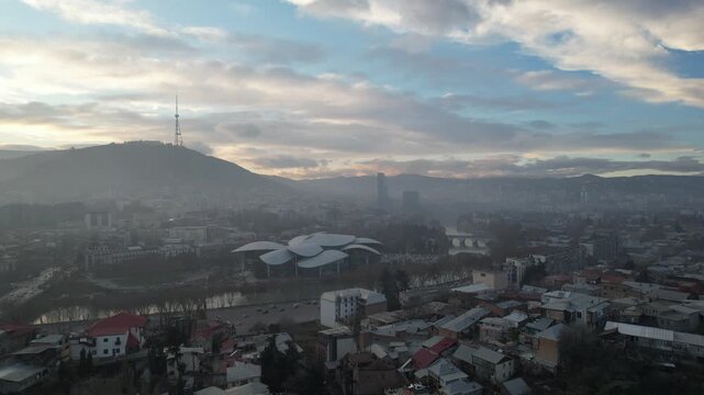 Aerial view of city center in Tbilisi at dusk, flying above the Mtkvari Kura River. Warm sunset light and calm evening atmosphere. High-quality 4K footage.