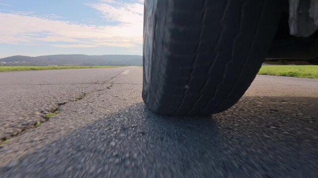 POV drive video from an action camera near the wheel, showing a car tire rolling on an open road in daylight. Dynamic low-angle perspective, travel, motion, speed, and transportation concept