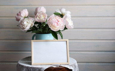 bouquet of delicate pink peonies in enameled jug and an empty frame. spring mockup with place for text