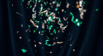 Scattered green and silver star confetti and ribbon pieces on a dark background, representing celebration, party, or festive occasion