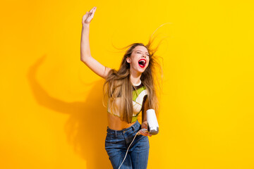 Vibrant Young Woman Laughing Joyfully on a Bright Yellow Background Holding a Hair Dryer,...