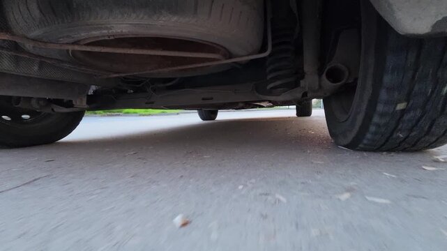 POV drive video from an action camera mounted under a car, showing undercarriage, wheels and suspension moving over a wet road. Dynamic automotive motion, speed, vehicle mechanics and transportation