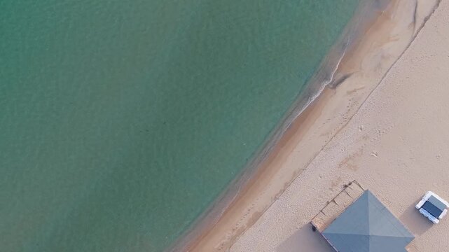 Top down drone view of sandy beach and green sea water with gentle waves creating natural coastal patterns textures movement.
