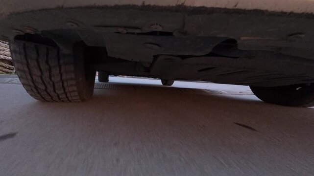 POV drive video from an action camera mounted under a moving car, showing undercarriage and wheels on urban asphalt. Low-angle automotive motion, speed, vehicle mechanics and transportation concept