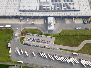 Aerial view of a large logistics warehouse with loading docks and trucks, distribution center surrounded by farmland. Supply chain and transportation concept
