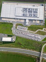 Aerial view of a large logistics warehouse with loading docks and trucks, distribution center surrounded by farmland. Supply chain and transportation concept