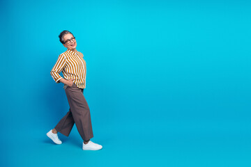 Aged female model in striped shirt and brown pants smiling against blue background