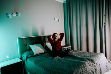 Naklejka premium Young woman studying on bed with laptop in bedroom during evening