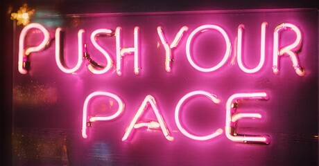 Bright pink neon sign displays motivational phrase push your pace. Dark background emphasizes glowing text. Simple, bold lettering.