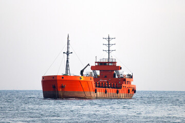 Fototapeta premium Close-up of bright orange offshore supply vessel with crane, safety gear, and communication masts—framed by calm sea and soft daylight in a specialized maritime logistics and engineering scene.