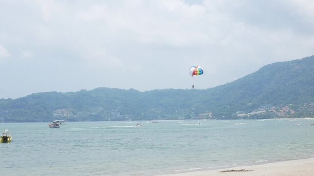 view to beach sea with parachute paragliding under summer vacation holiday time at patong bay beach. Extreme freedom sport activity at tropical sea beach vacation