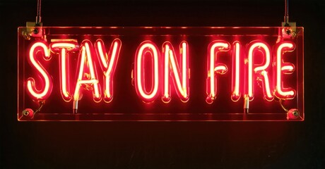 Fototapeta premium Bright red neon sign displays text Stay on Fire. Dark background emphasizes glowing illumination. Simple, bold message.