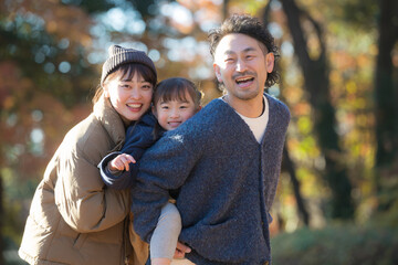 Fototapeta premium 秋の公園で遊ぶ家族 お出かけやレジャーのイメージ おんぶで仲良しファミリー カメラ目線
