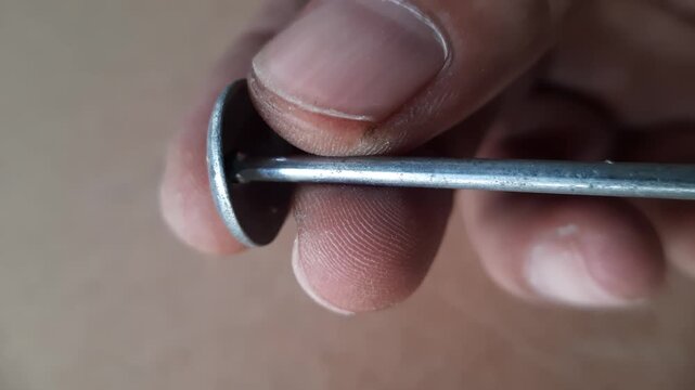 Human hand holding a silver zinc roofing nail with a wide round head and a sharp pointed tip shown in a detailed macro shot