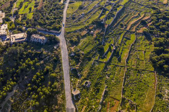 Aerial view of a winding road cutting through the contrasting green and brown fields, leading the eye towards the horizon, Mellieha bay, Malta.