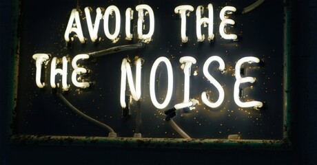 Neon sign displays text. Words avoid the noise glow brightly against dark background. Rustic frame adds texture.