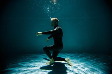 Fototapeta premium Free diver in wetsuit holding breath while training underwater in pool
