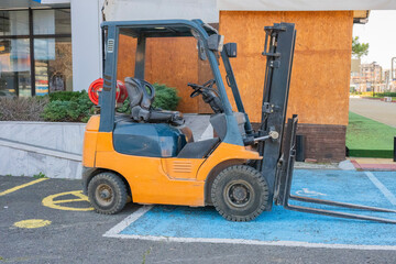 a yellow forklift truck parked on a painted blue rectangular area on asphalt, positioned in front of a wooden shed structure. © Andrey