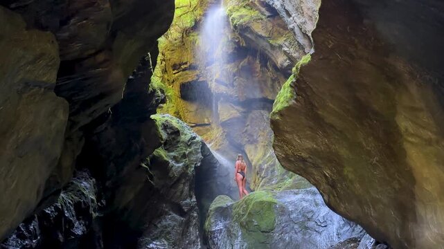 A girl walks out onto a rocky platform inside Wilsons Creek Chasm, Haast Pass, New Zealand. Towering cliffs and rushing water surround this dramatic and scenic gorge.