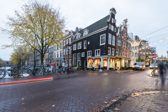 View of the wet cobblestone street reflecting the warm glow of shops nestled in historic buildings at night, Amsterdam, North Holland, Netherlands.