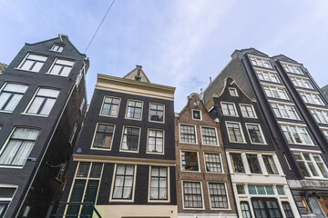 View of tall, narrow, historic buildings stand shoulder-to-shoulder, their dark brick facades contrasting with bright window frames, Amsterdam, North Holland, Netherlands.
