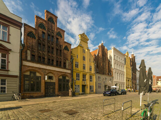 View of gabled buildings with intricate brickwork and vibrant colors lining a cobblestone street under a blue sky with fluffy clouds, Stralsund, Mecklenburg-Vorpommern, Germany.