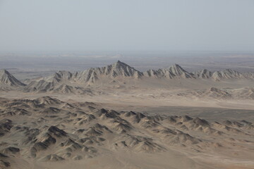 Aerial view of rugged, sun-baked mountains and arid plains stretch into the hazy horizon, painted in earthy browns and muted tans, Reko Diq, Balochistan, Pakistan.