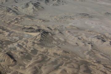 Aerial view of rugged, arid mountains and valleys stretch under a hazy sky, the stark landscape revealing a tapestry of textures in muted browns and greys, Reko Diq, Balochistan, Pakistan.