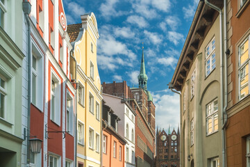 View of colorful buildings rise with intricate facades under a sky streaked with clouds, leading to a distant church spire, Stralsund, Mecklenburg-Vorpommern, Germany.