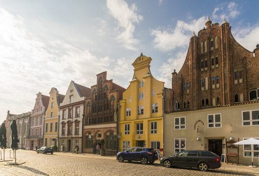 View of colorful buildings stand in a row under a bright sky, cars parked in front of the buildings in old town, Stralsund, Mecklenburg-Vorpommern, Germany.