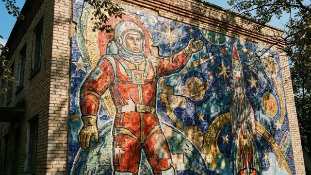 Man cosmonaut mosaic art on building. Soviet space era mural on brick wall. Outdoor cultural monument with rocket and planet imagery.