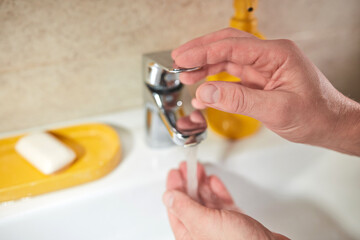 Human hands are turning the home faucet on and washing it with soap and clean tap water for good...