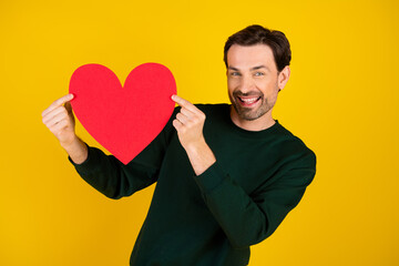 Happy man holds red heart cutout against yellow background for love friendship and positive vibes...