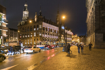 Amsterdam, Netherlands - 19 November 2016: View of the illuminated Beurs van Berlage and Dam Square at night, where the wet cobblestones shimmer under the streetlights.