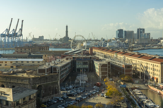 Genoa, Italy - 27 December 2022: View of the harbor with its cranes, the iconic Lanterna lighthouse, and the Ferris wheel, all bathed in the soft glow of the afternoon sun.
