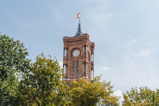 Berlin, Germany - 28 August 2019: View of the Rotes Rathaus tower, a brick structure with a clock, topped with the Berlin flag against a soft, blue sky.
