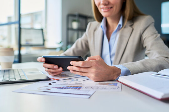 Businesswoman using smartphone at desk with financial reports in office