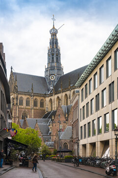Haarlem, Netherlands - 06 May 2019: View of the majestic Grote Kerk rising above the street, its spire piercing the overcast sky, framed by the linear facades of buildings.