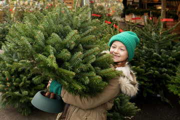 Girl choosing Christmas tree outdoors at forestry market