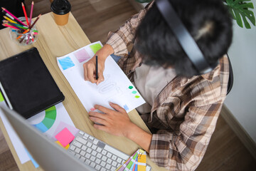 Designer Wearing Headphones and Plaid Shirt, Working at Desk on Product Sketches