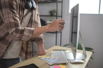Closeup of Graphic Designer's Hand Using Stylus on Screen With Color Swatch Fans on Desk