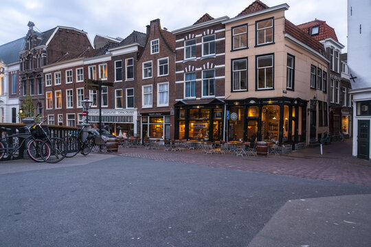 Leiden, Netherlands - 05 May 2019: View of the vibrant street corner, where the warm glow of the cafe spills onto the cool, grey pavement, contrasting against the dark brick facades.