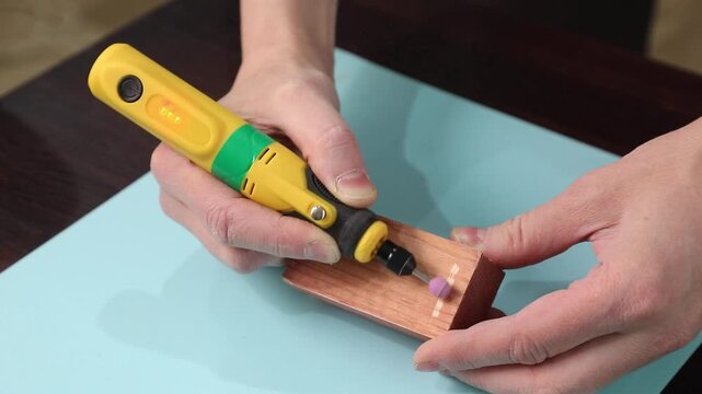 Person using hand engraving tool with ceramic tip on painted wooden block. Craft workshop concept.